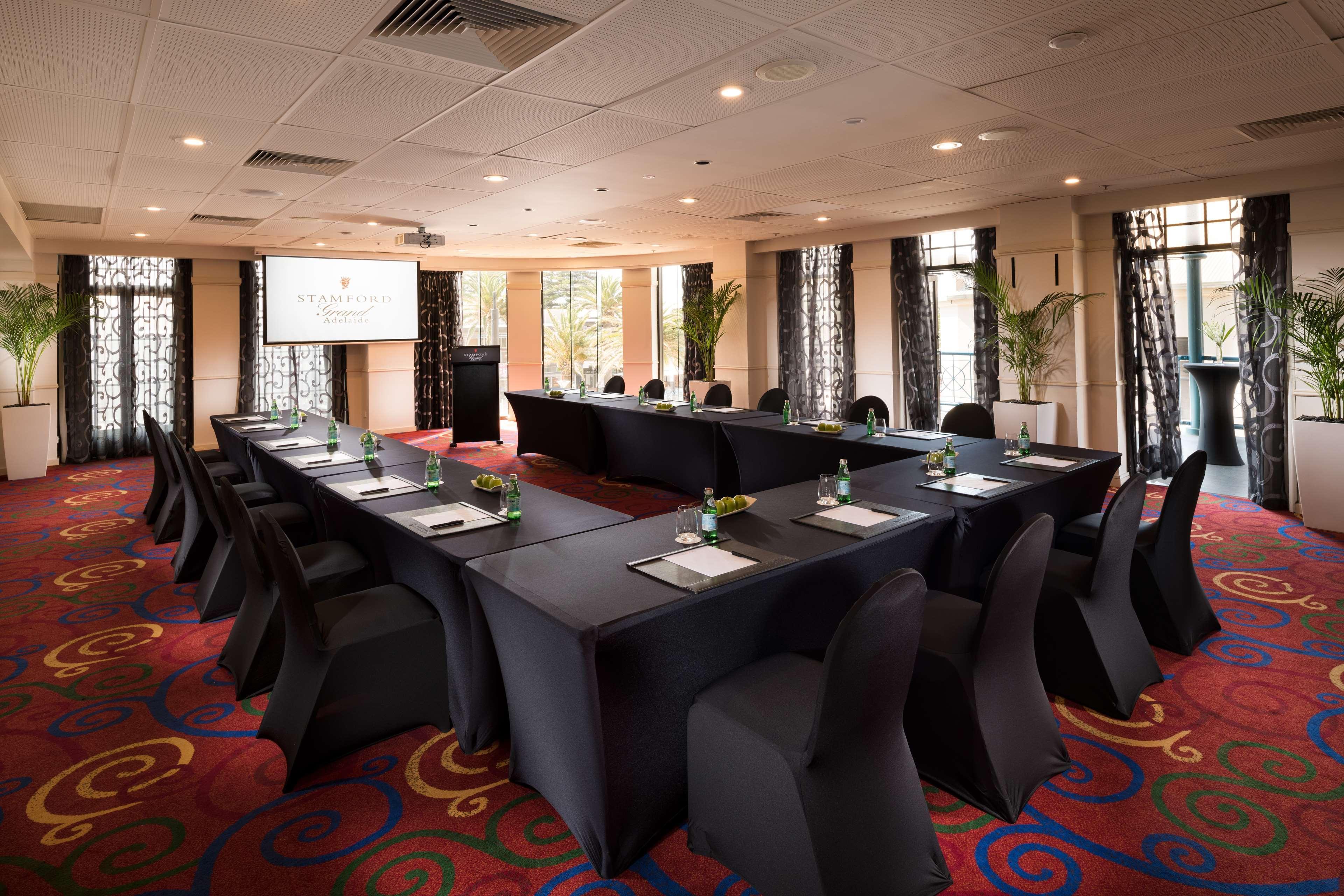 Hotel Stamford Grand Adelaide Glenelg Esterno foto The photo shows a conference room set up for a meeting or presentation. There are several tables arranged in a U-shape, covered with black tablecloths. Each table has a notepad and a small bottle of water on it. The chairs around the tables are also 