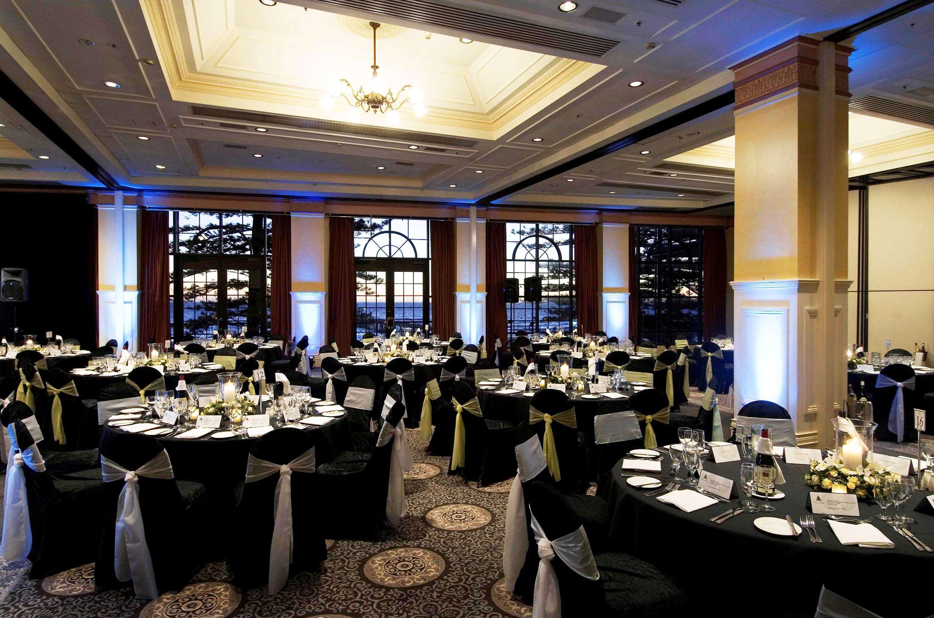 Hotel Stamford Grand Adelaide Glenelg Ristorante foto The photo depicts an elegantly arranged banquet hall set for an event. The room features round tables covered with black tablecloths, each adorned with white tableware and floral centerpieces. Chairs are draped in white fabric with decorative sashes 