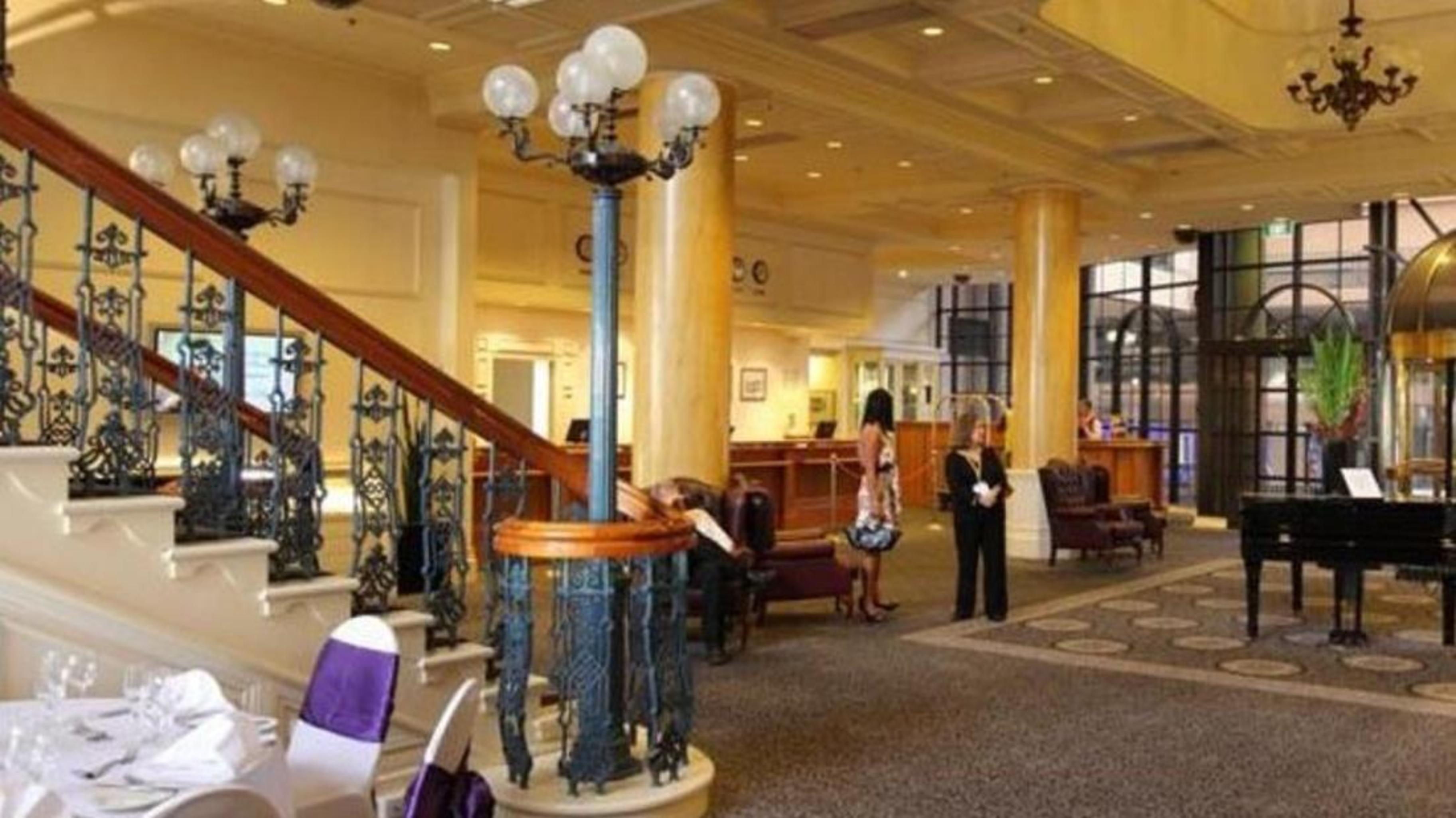 Hotel Stamford Grand Adelaide Glenelg Esterno foto The photo shows the interior of a hotel lobby. It features a spacious area with a high ceiling and elegant decor. There is a staircase with a decorative railing leading to an upper level. In the foreground, some guests and staff are present, and ther