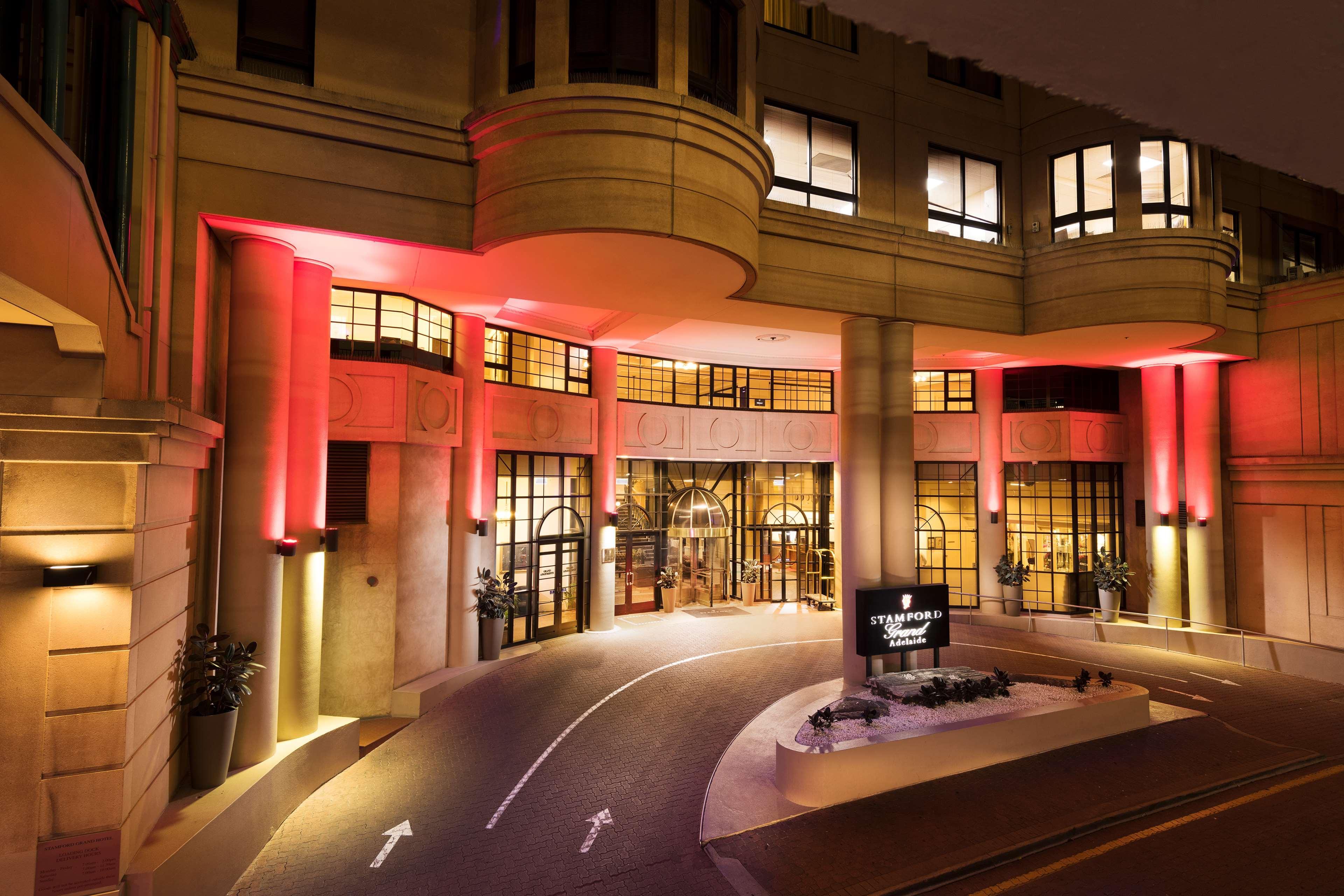 Hotel Stamford Grand Adelaide Glenelg Esterno foto The photo shows the entrance of a hotel or luxury building at night. The façade features a modern architectural style with large windows and an elegant entrance. The area is illuminated with red lighting, creating an inviting atmosphere. There appear