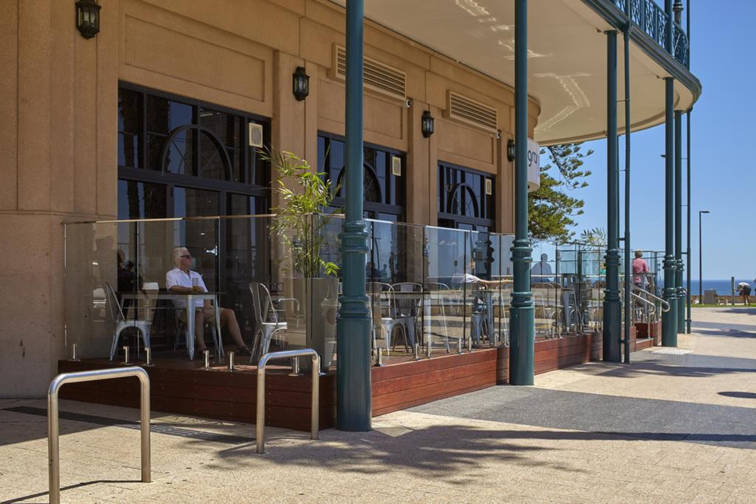Hotel Stamford Grand Adelaide Glenelg Esterno foto The photo shows the exterior of a cafe or restaurant with a large outdoor seating area. There are glass barriers around the seating, providing a view of the outside while maintaining a sense of enclosure. The building has a modern architectural style