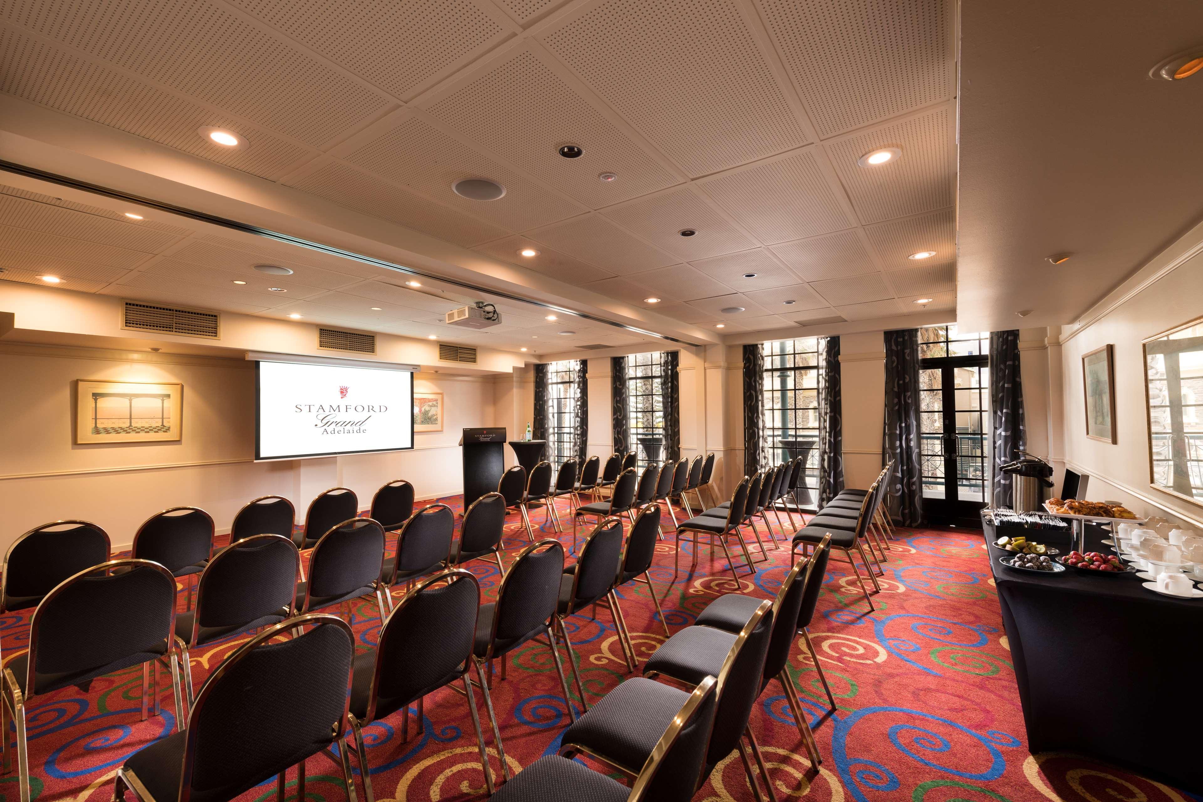 Hotel Stamford Grand Adelaide Glenelg Esterno foto The photo shows a conference room set up for an event. There are rows of black chairs arranged in a semicircular formation facing a presentation screen at the front. The room features large windows that allow natural light to enter, and the flooring 
