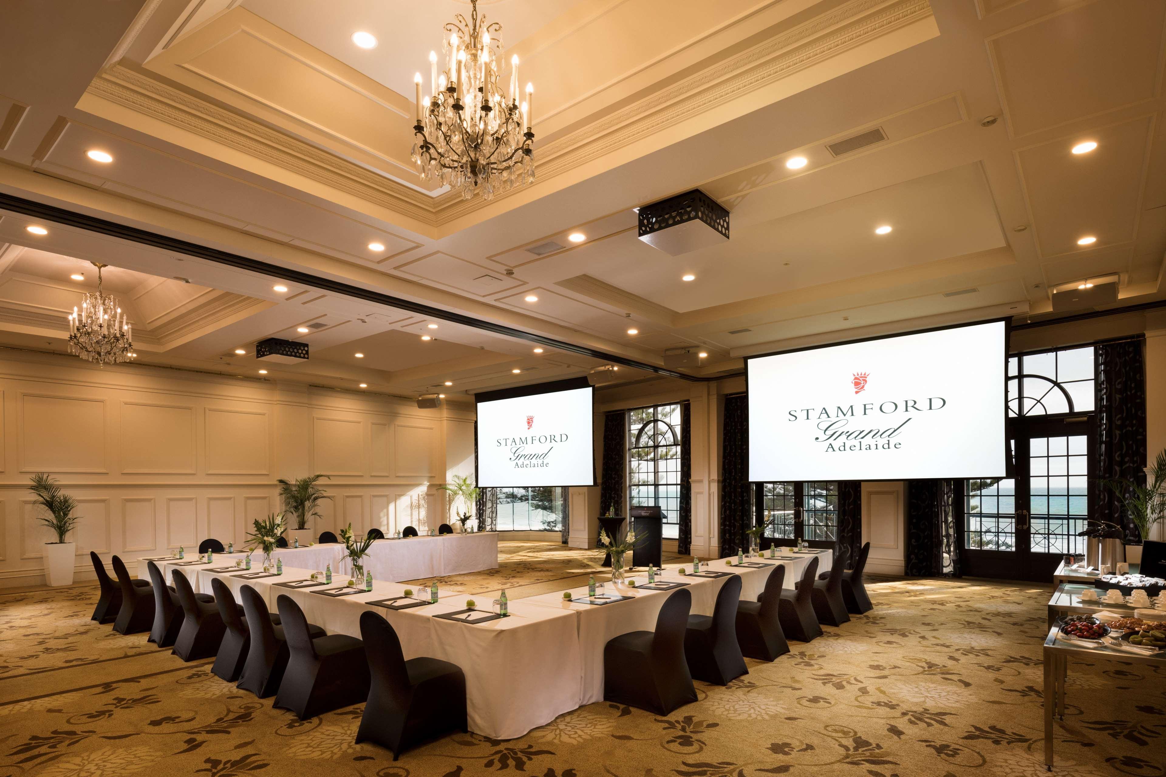 Hotel Stamford Grand Adelaide Glenelg Esterno foto The photo shows a spacious and elegantly designed conference room. The room features a long table set for a meeting, surrounded by stylish chairs. Two large screens are positioned at the front, displaying the logo "Stamford Grand Melbourne." The ceil