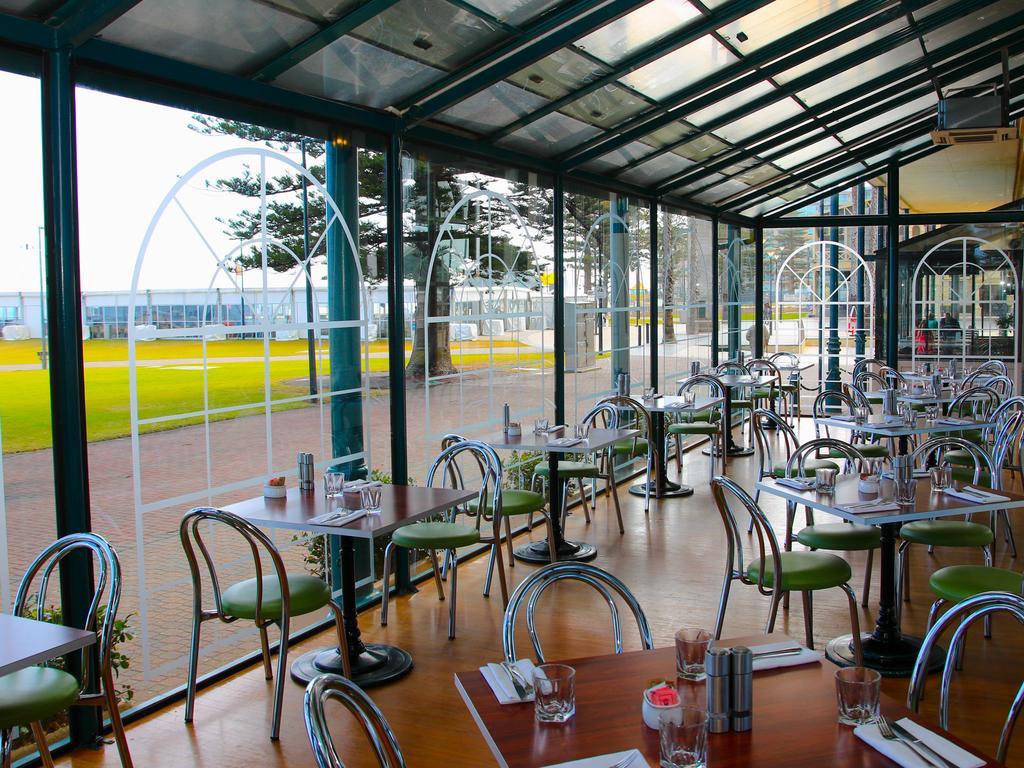Hotel Stamford Grand Adelaide Glenelg Esterno foto The photo shows the interior of a restaurant with a modern design. The space features several tables with green chairs, arranged in a way that allows for ample seating. Large glass windows provide a view of the outside, creating a bright and open atm